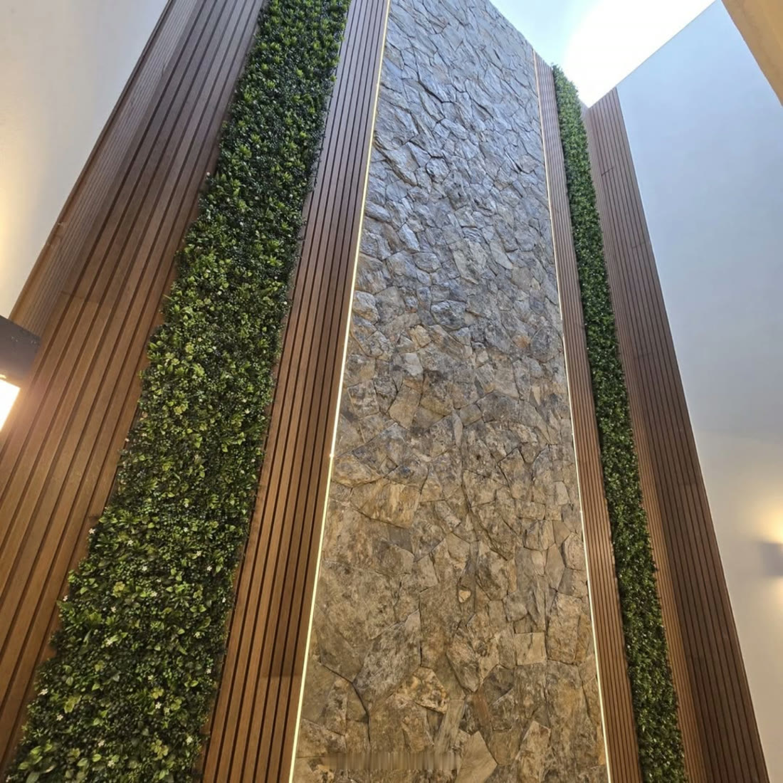 Interior de doble altura de Casa Andrea's 20 con muro de piedra, duela de madera y jardines verticales